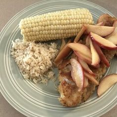 a plate with chicken, rice, and apple slices on it next to an ear of corn