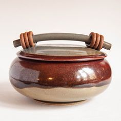 a brown and white ceramic pot with a wooden handle on it's side, sitting on a white surface