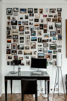 a desk with a computer on top of it in front of a wall full of pictures