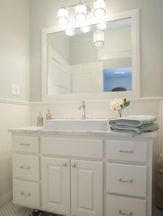 a bathroom with white cabinets and a large mirror above the sink is lit by three lights