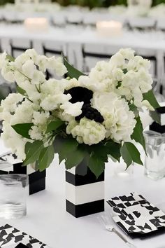 white flowers in black and white vases on a table with place settings for dinner