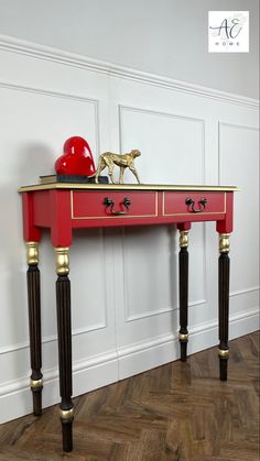 a red table with black legs and an apple on top, against a white wall