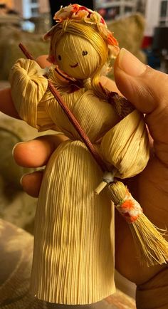 a person holding a small doll made out of yellow material with orange flowers on it's head