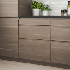 a kitchen with wooden cabinets and plants on the counter top, in front of a white tile backsplash