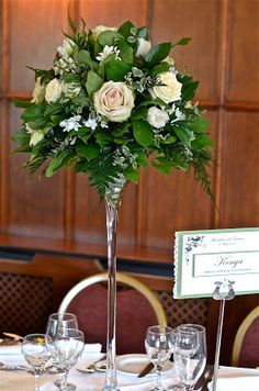 a tall vase filled with white flowers sitting on top of a table next to wine glasses