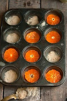 there are many oranges in the muffin tins on the wooden table with utensils