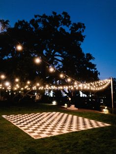 a checkerboard dance floor is lit up at night with fairy lights strung over it