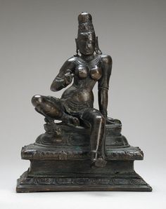 a bronze statue sitting on top of a stone slab in front of a gray background