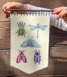 a woman is holding up a wall hanging with four bugs on it and one bug in the middle