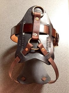 a helmet made out of metal and leather on top of a white table with a brown strap