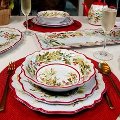 the table is set with red place mats and white plates, silverware, and wine glasses