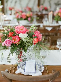 an arrangement of flowers in a vase on a table with place settings and napkins