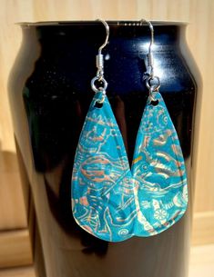 a pair of blue and white earrings sitting on top of a black vase in front of a wooden wall