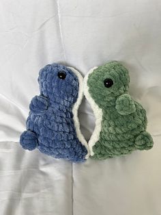 two small stuffed animals laying on top of a bed next to each other, one is green and the other is blue