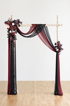 an arch decorated with red and black flowers on top of a hard wood floor in front of a white wall