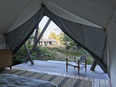 a bed sitting under a tent on top of a wooden floor next to a forest