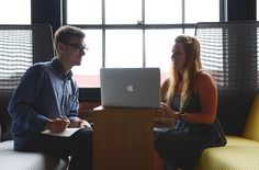 a man and woman sitting in front of a laptop on a yellow chair next to each other