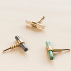 three pairs of gold and green ear studs on a white surface, one with two different colored stones