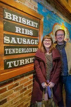 two people standing next to each other in front of a brick wall with signs on it