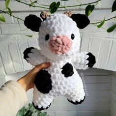 a hand holding up a small white and black cow stuffed animal next to a brick wall