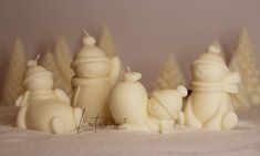 some white candles are lined up in the snow with trees around them and one candle has a teddy bear on it