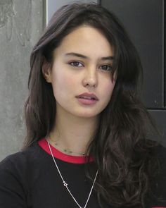 a young woman with long hair wearing a black shirt and silver necklace looking at the camera