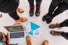 several people standing in a circle with their feet on the ground and looking at a laptop