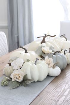 a wooden table topped with white pumpkins and flowers