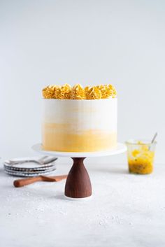 a white cake with yellow frosting on a wooden stand next to other desserts and utensils