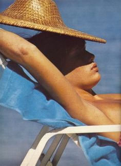 a woman in a straw hat laying on a beach chair with her arms behind her head