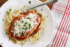 spaghetti with sauce and parmesan cheese on a white plate next to a fork