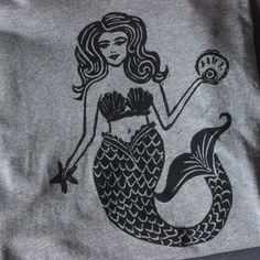 a gray shirt with a black mermaid on it's chest and a clock in her hand