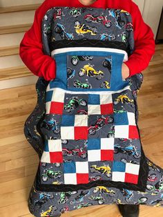 a young boy is holding up a quilted car seat cover that has cars on it