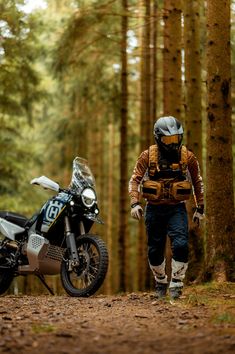 a man walking next to a motorcycle in the woods