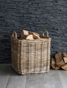 a wicker basket with wood logs on the floor in front of a brick wall