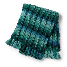 a green and blue knitted blanket laying on top of a white surface with tassels