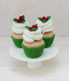 three cupcakes with white frosting and crochet decorations on a plate