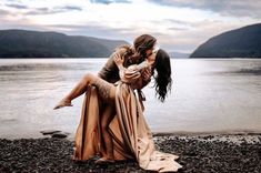 two people are hugging on the shore of a lake