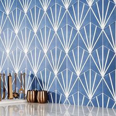 a blue and white wall with gold vases next to it on a counter top