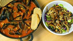 there is a bowl of food next to a bowl of salad on the table with bread