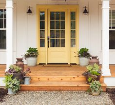 a yellow front door with potted plants on the steps