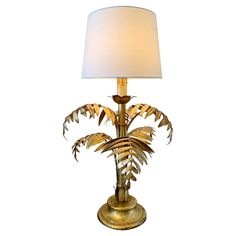 a table lamp with a white shade on the top and a gold metal plant design