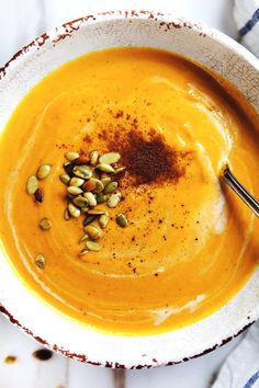 a white bowl filled with carrot soup and topped with pumpkin seeds, cinnamon sprinkled on top