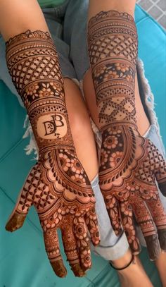 two hands with henna tattoos on them, one is showing the letter b and the other