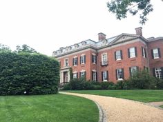 a large red brick house sitting on top of a lush green field next to a sidewalk