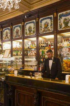 a man in a tuxedo is behind the bar at a fancy restaurant,