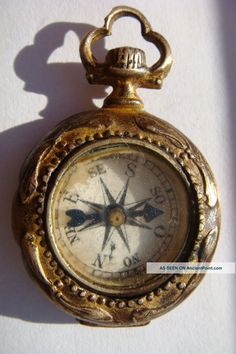 an old gold pocket watch with compass on the front and back side, sitting on a white surface