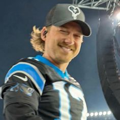 a man in a baseball cap smiles while standing next to a giant tire on the field