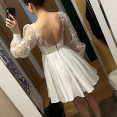 a woman taking a selfie in front of a mirror wearing a white dress with long sleeves