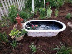 an old bathtub is filled with water and flowers in the garden next to a fire hydrant